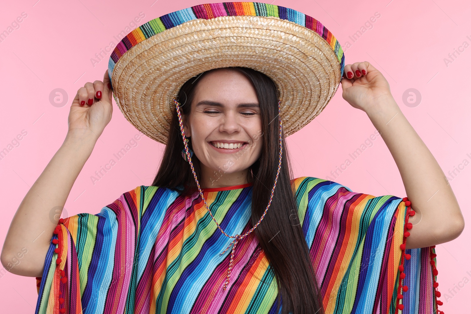 Photo of Young woman in Mexican sombrero hat and poncho on pink background