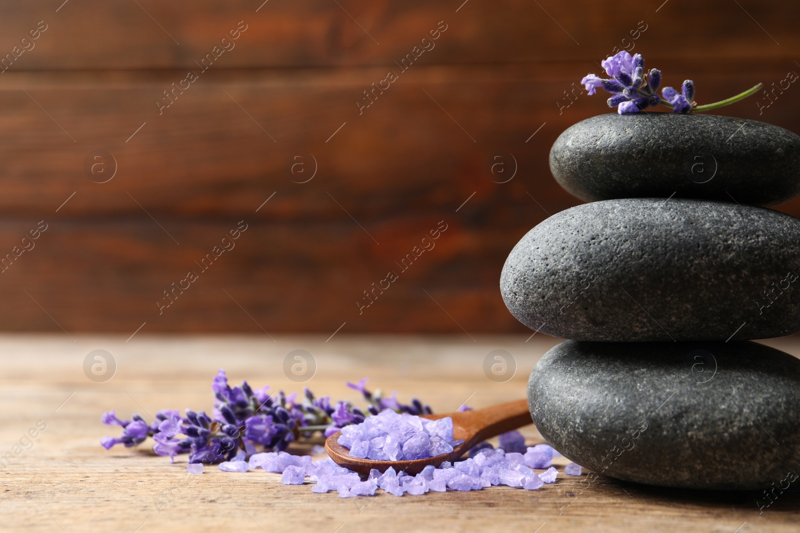 Photo of Spa stones, natural cosmetic bath salt and lavender flowers on wooden table, space for text