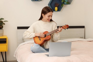 Happy young woman learning to play ukulele with online music course via laptop at home. Time for hobby
