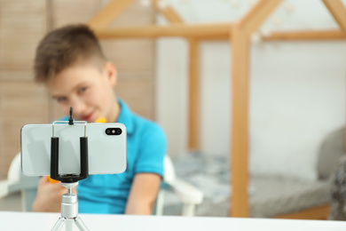 Photo of Cute little blogger with toy recording video at home, focus on phone