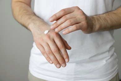 Photo of Man applying cream onto hand against grey background, closeup