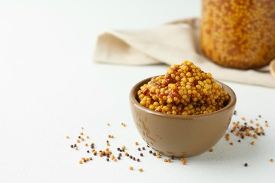 Photo of Fresh whole grain mustard in bowl and dry seeds on white table. Space for text