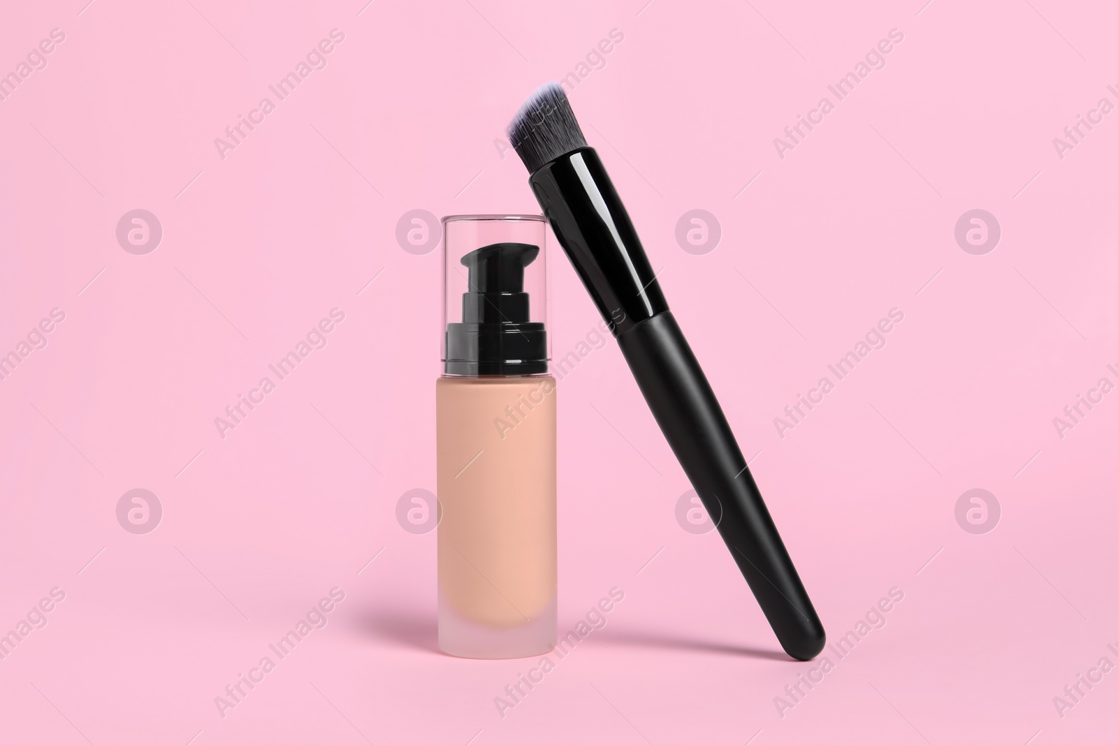 Photo of Bottle of skin foundation and brush on pink background. Makeup product