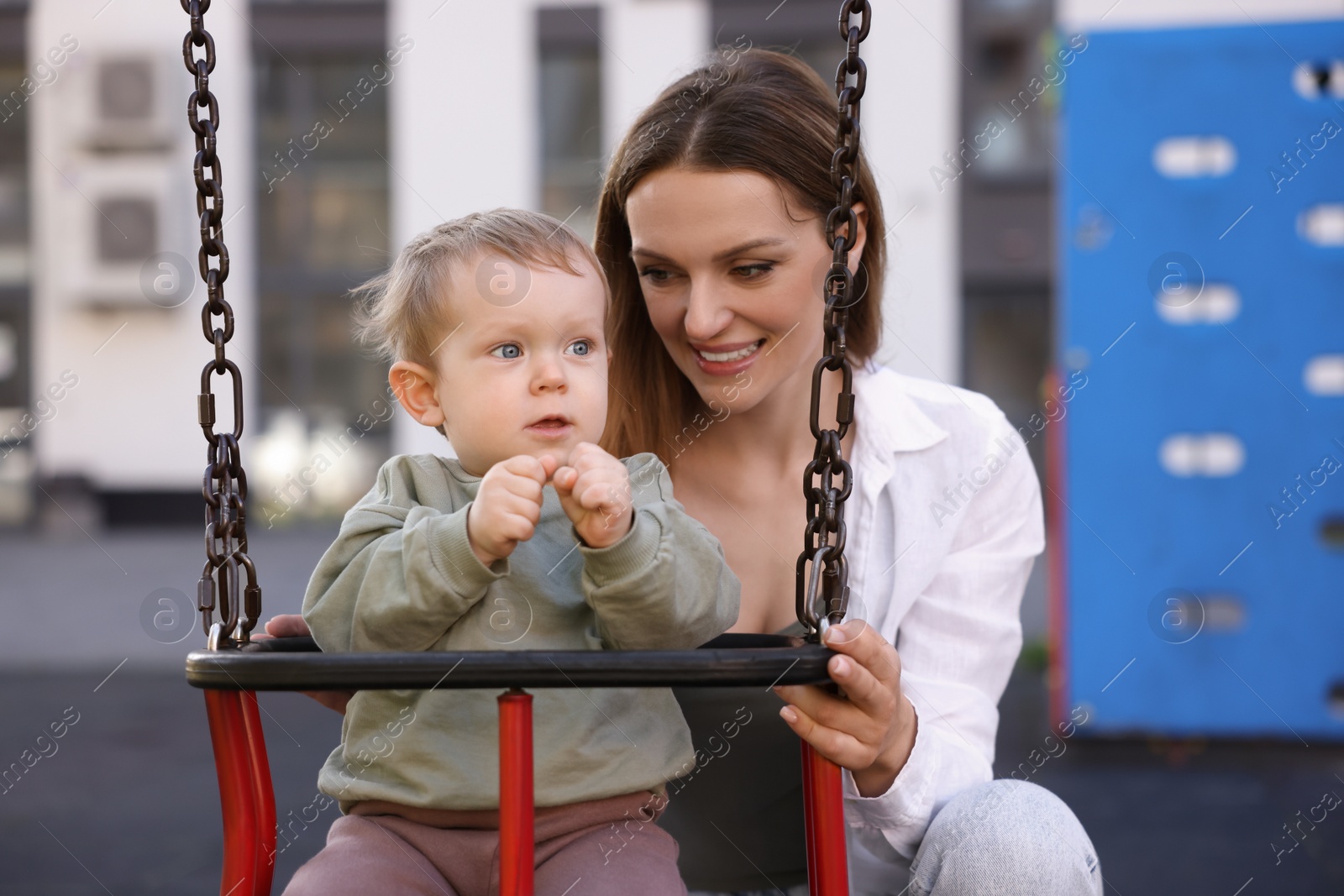 Photo of Happy nanny and cute little boy on swing outdoors