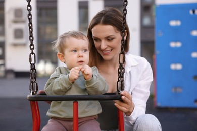 Happy nanny and cute little boy on swing outdoors