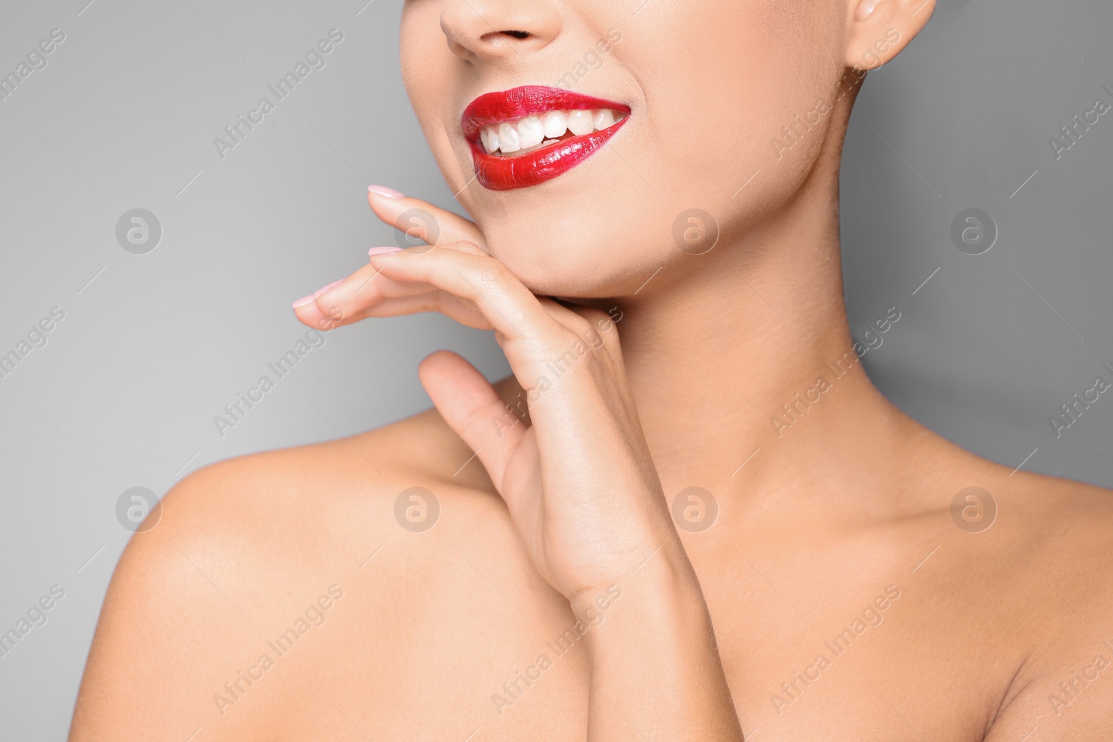 Photo of Beautiful young woman with red glossy lips on gray background, closeup