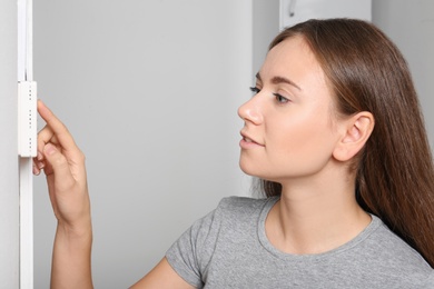 Woman adjusting thermostat on white wall. Heating system