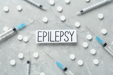 Photo of Sheet of paper with word Epilepsy, pills and syringes on grey marble table, flat lay