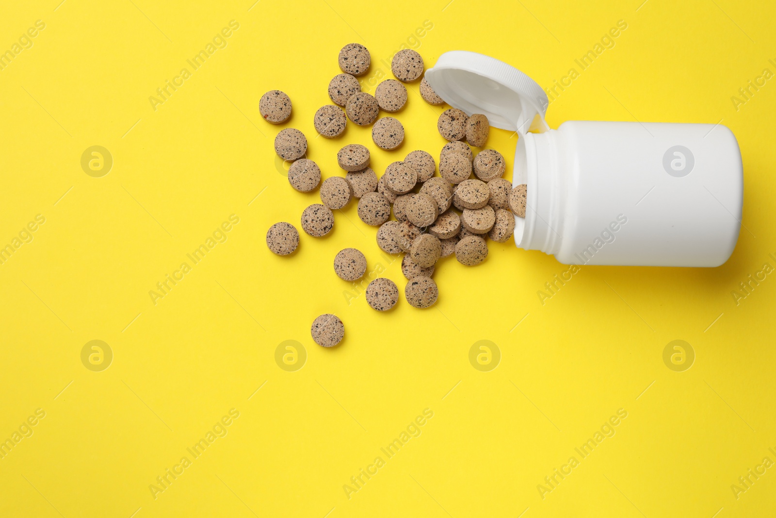 Photo of Vitamin pills and bottle on yellow background, top view. Space for text