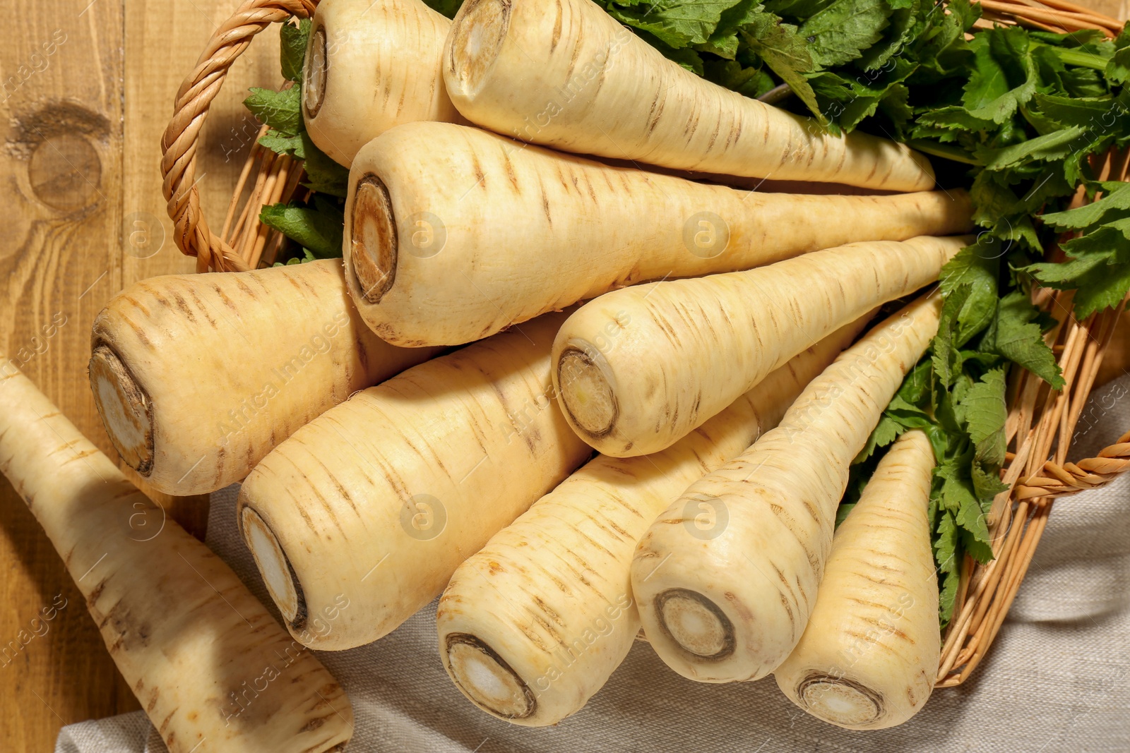 Photo of Wicker basket with delicious fresh ripe parsnips and green leaves on wooden table, above view