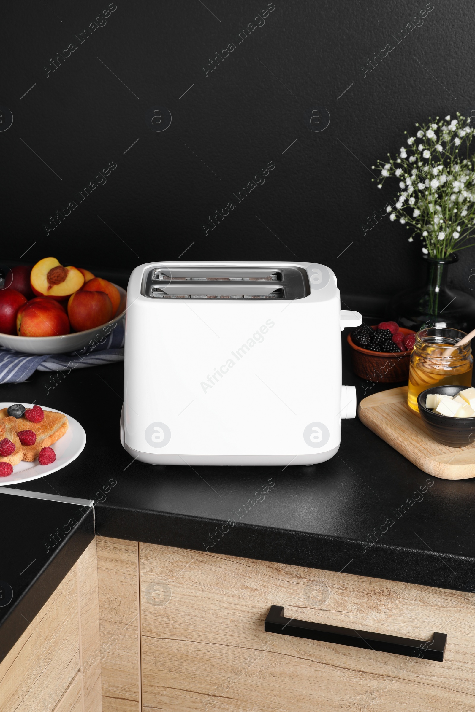 Photo of Modern toaster, bread, fresh berries and honey on countertop in kitchen