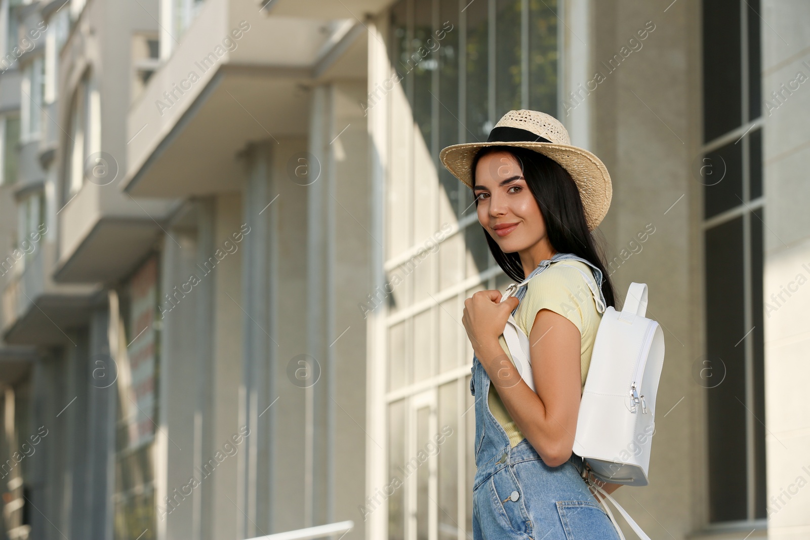 Photo of Beautiful young woman with stylish white backpack on city street, space for text