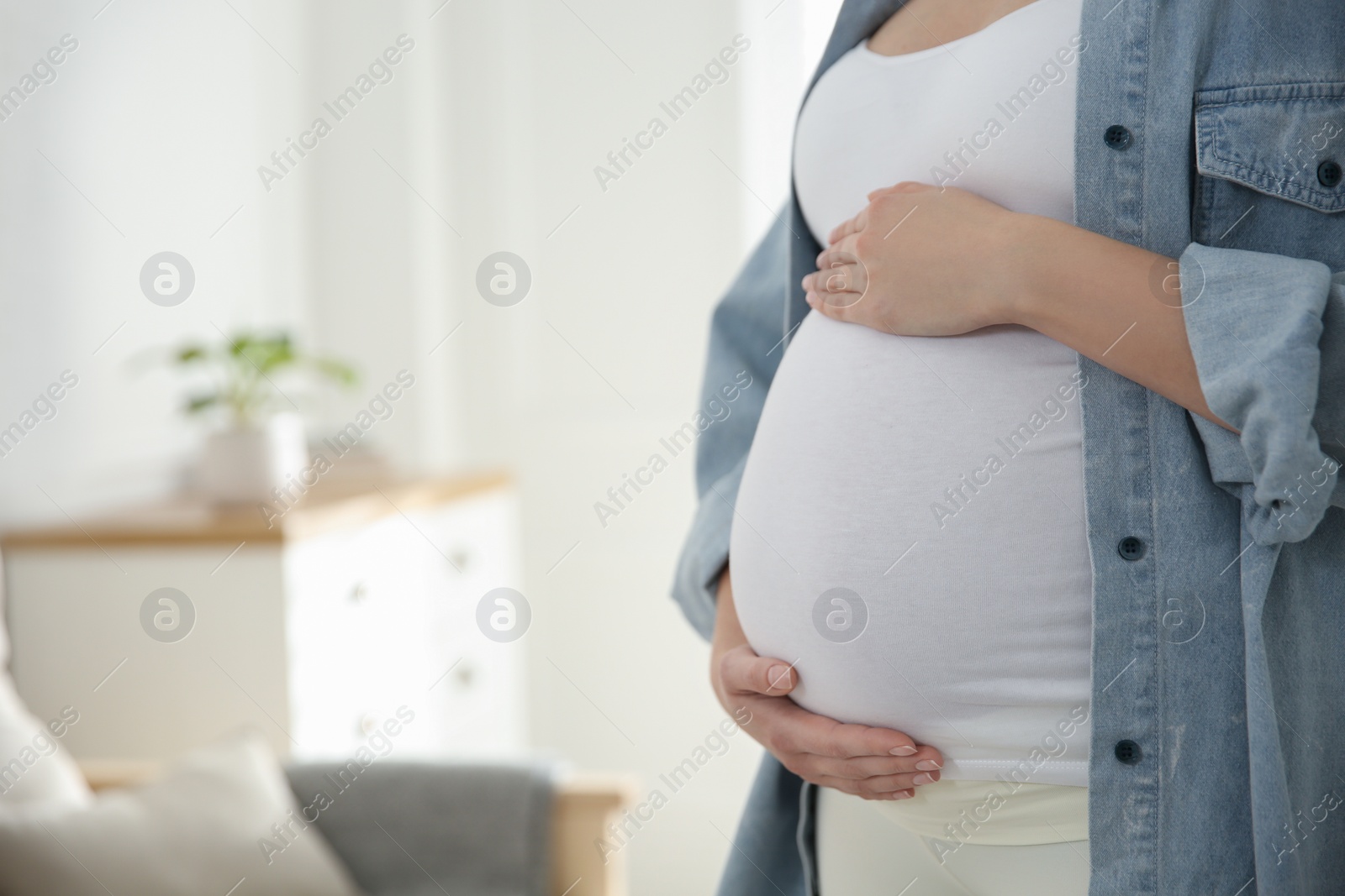 Photo of Pregnant woman touching her belly indoors, closeup