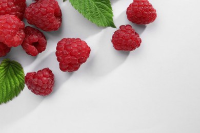 Photo of Tasty ripe raspberries and green leaves on white background, flat lay. Space for text