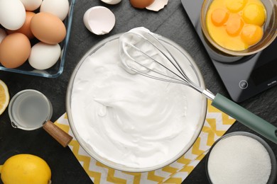 Bowl with whipped cream, whisk and ingredients on black table, flat lay