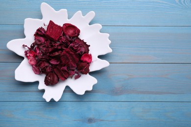 Aromatic potpourri of dried flowers in plate on light blue wooden table, top view. Space for text