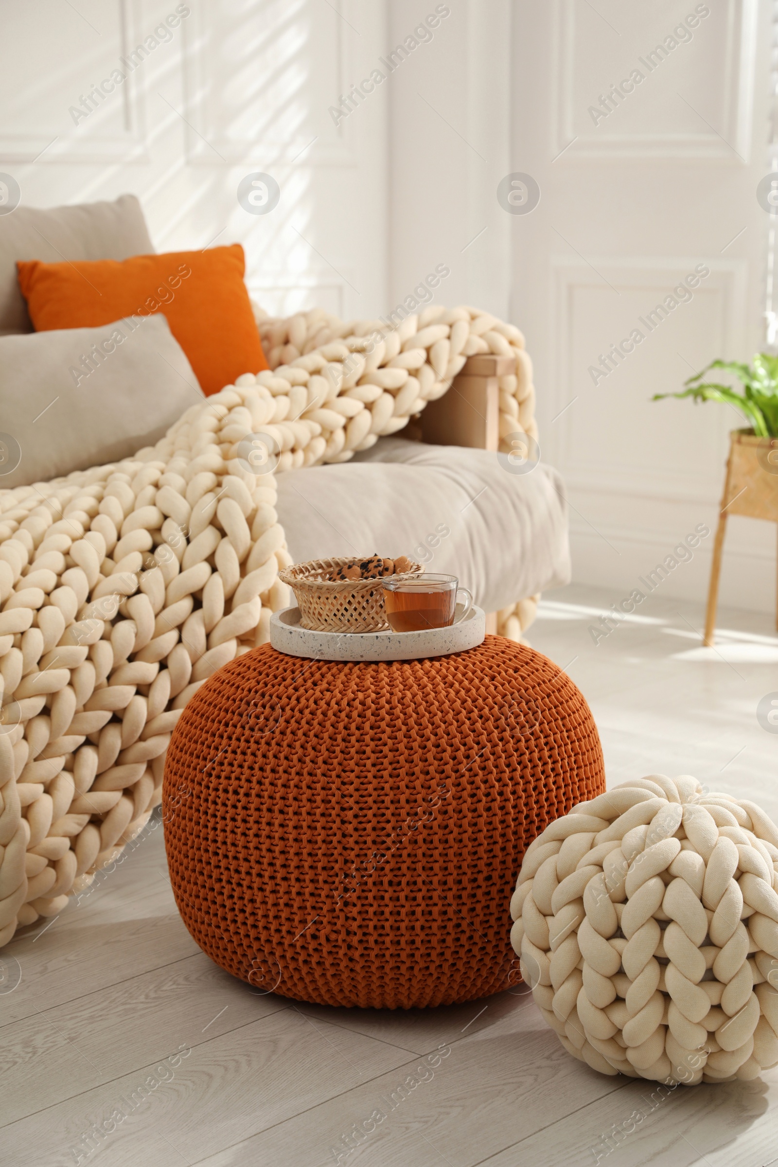 Photo of Tray with cup of tea and cookies on stylish comfortable pouf in room. Home design