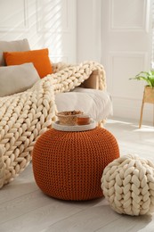 Tray with cup of tea and cookies on stylish comfortable pouf in room. Home design