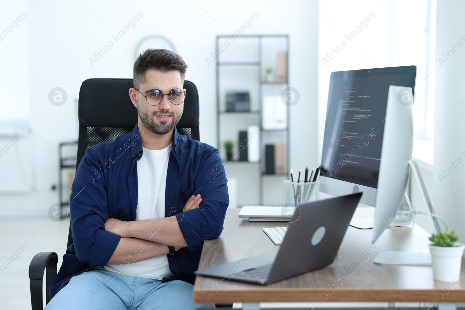 Photo of Happy young programmer working with laptop in office