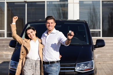 Happy couple with key near car on city street. Buying new auto