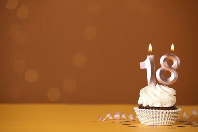 Photo of Coming of age party - 18th birthday. Delicious cupcake with number shaped candles on orange background, space for text