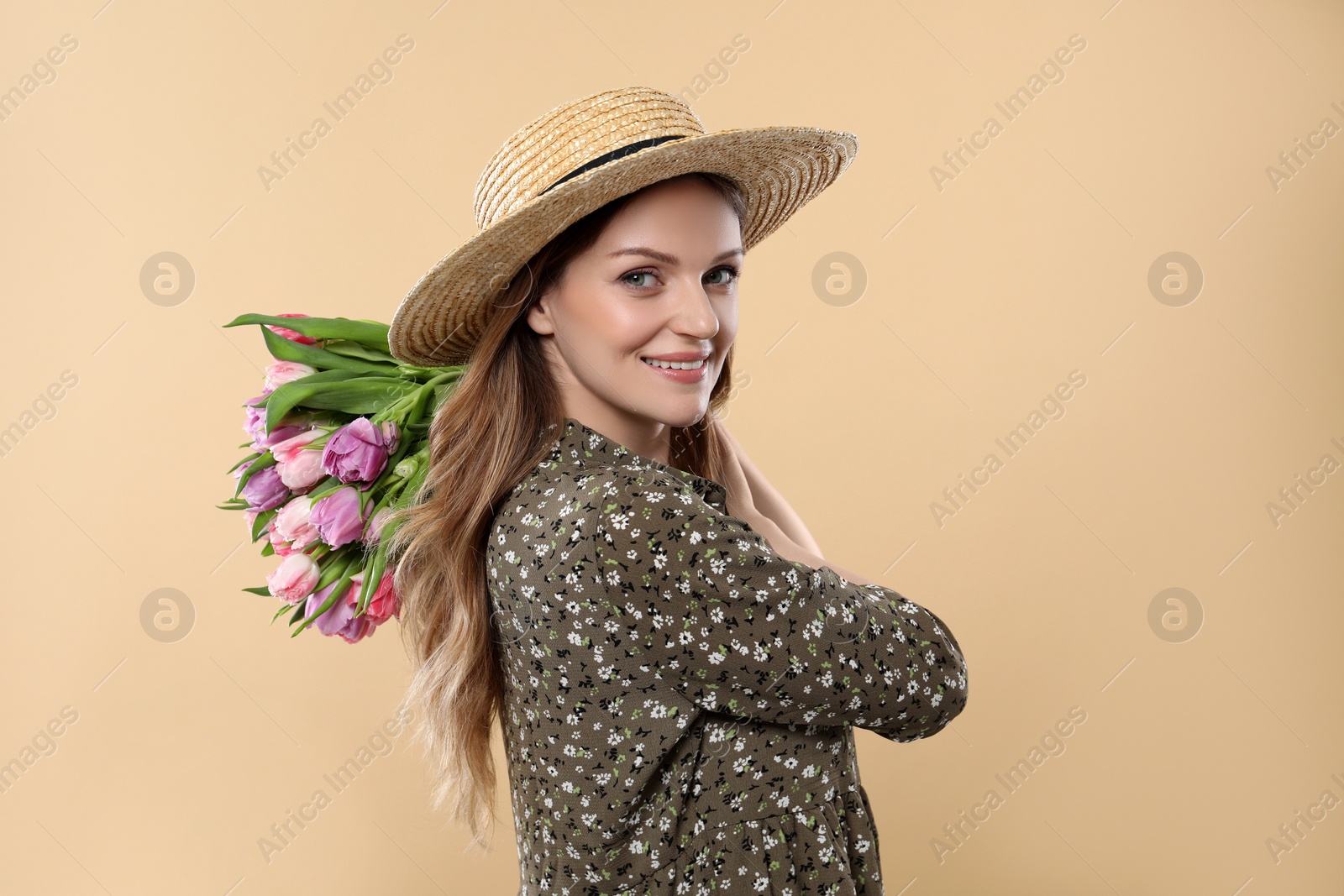 Photo of Happy young woman in straw hat holding bouquet of beautiful tulips on beige background