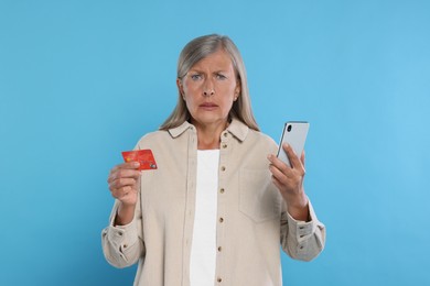 Photo of Worried woman with credit card and smartphone on light blue background. Be careful - fraud