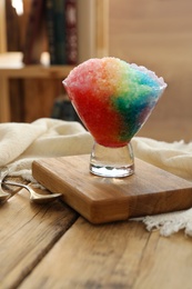 Photo of Rainbow shaving ice in glass dessert bowl on wooden  table indoors