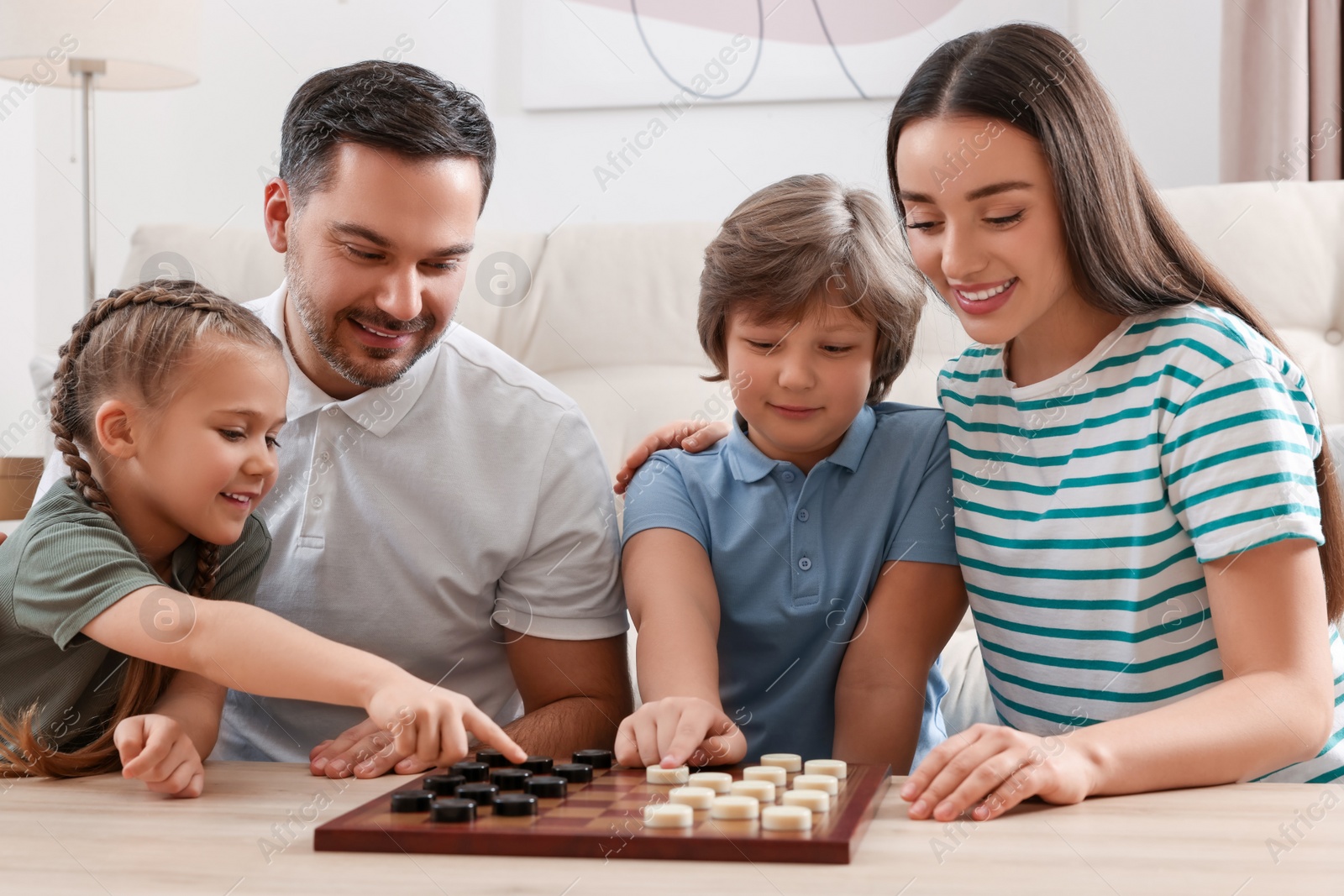 Photo of Parents playing checkers with children at table in room