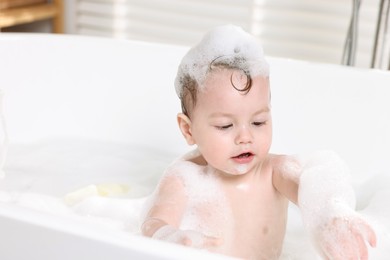 Photo of Cute little child bathing in tub at home, space for text