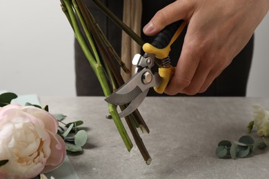 Photo of Florist cutting flower stems with pruner at workplace, closeup