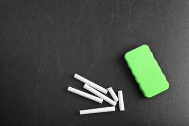 Photo of Pieces of chalk and duster on blackboard, top view