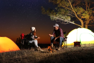 Photo of Couple near bonfire at night. Camping season