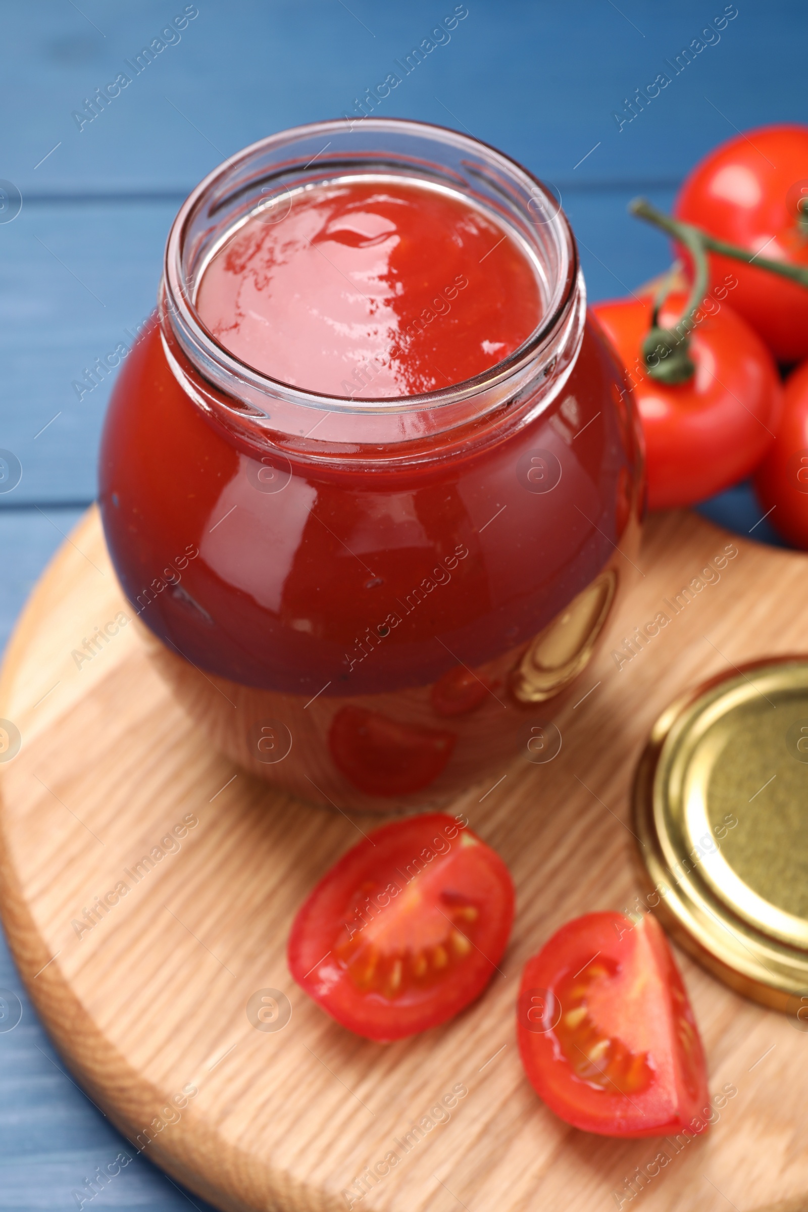 Photo of Organic ketchup in jar and fresh tomatoes on blue table. Tomato sauce