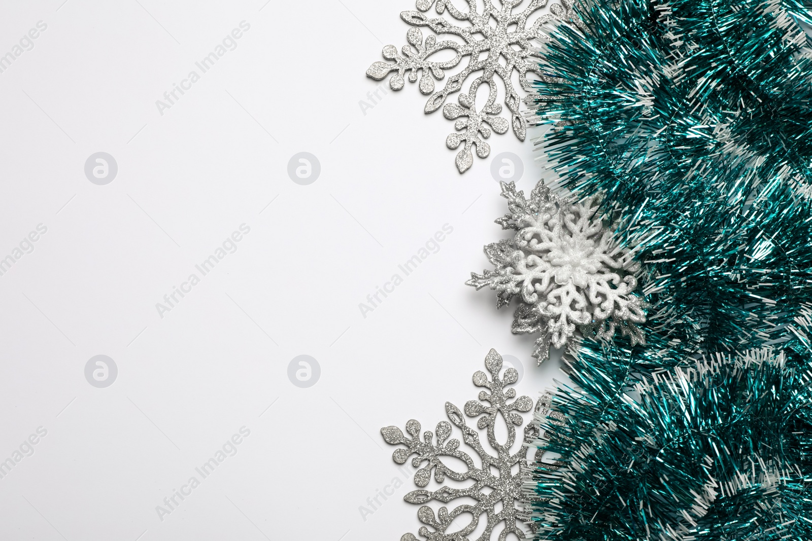 Photo of Bright tinsel and snowflakes on light background, flat lay. Space for text