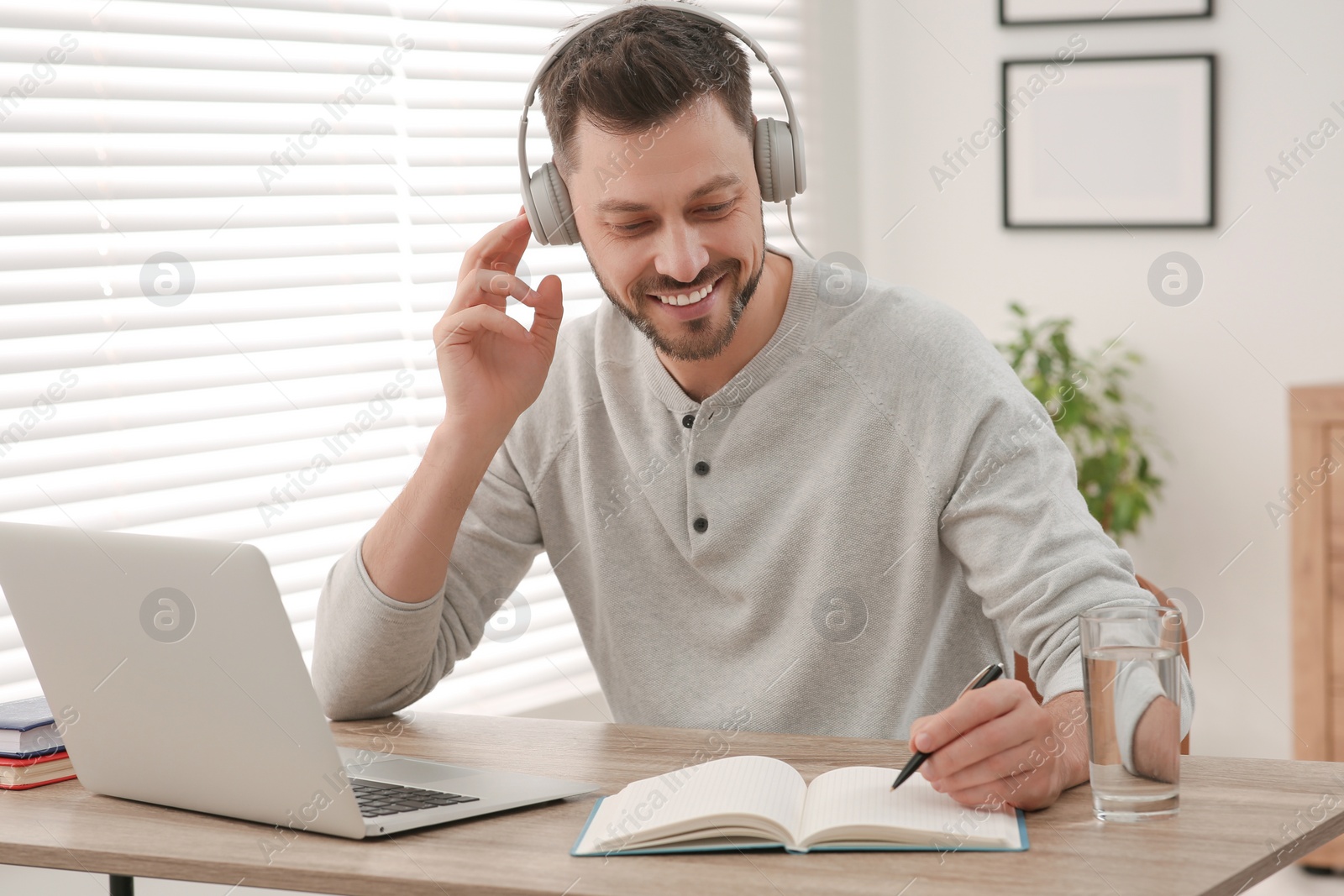 Photo of Online translation course. Man in headphones writing near laptop at home