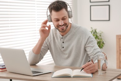 Photo of Online translation course. Man in headphones writing near laptop at home