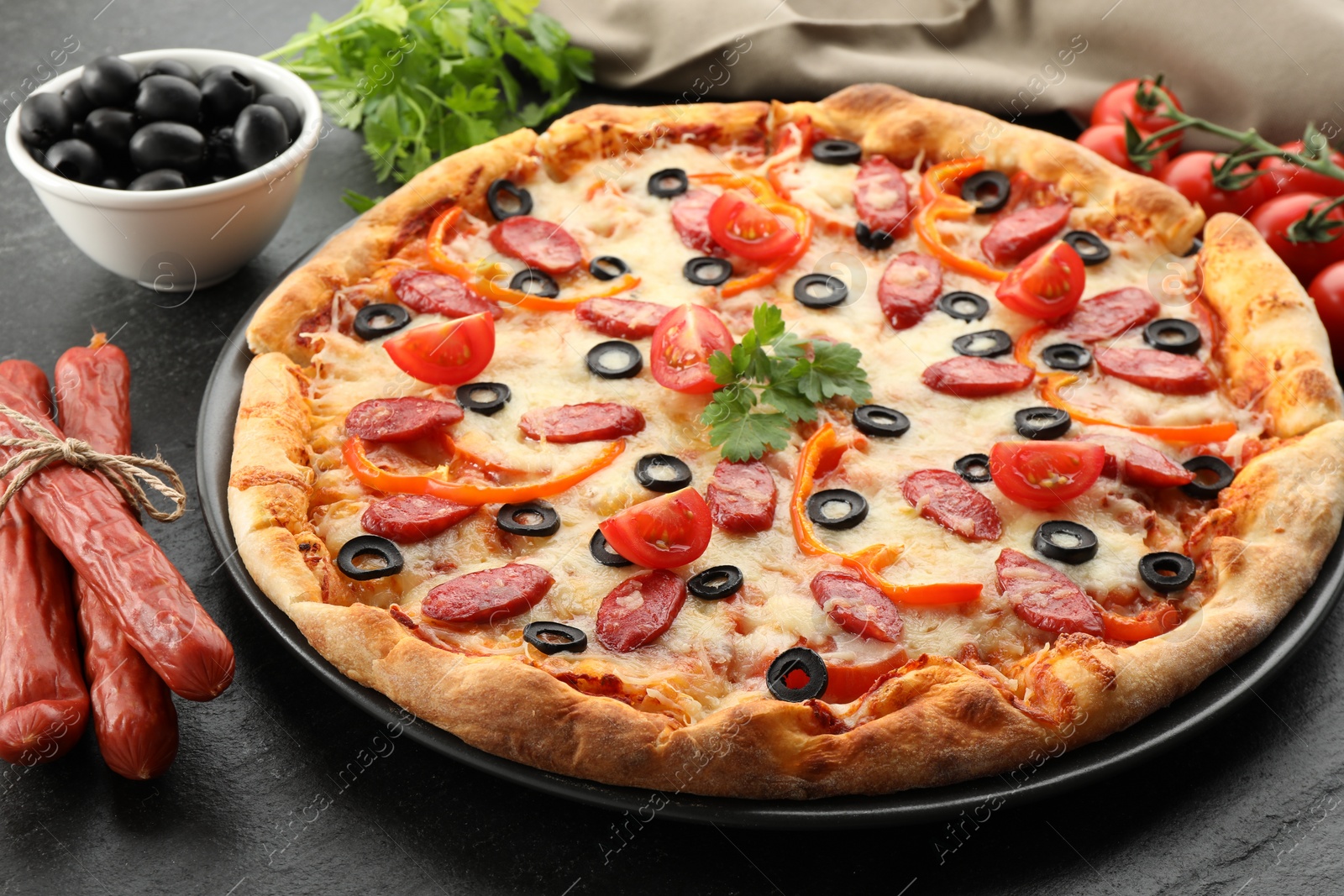 Photo of Tasty pizza with dry smoked sausages, olives, tomatoes, pepper and parsley on grey table