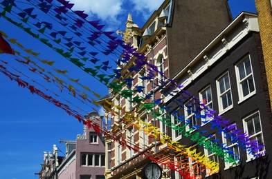 Bright rainbow bunting flags against blue sky, low angle view. LGBT pride concept