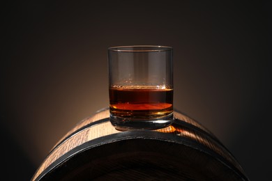 Photo of Glass of tasty whiskey on wooden barrel against dark background