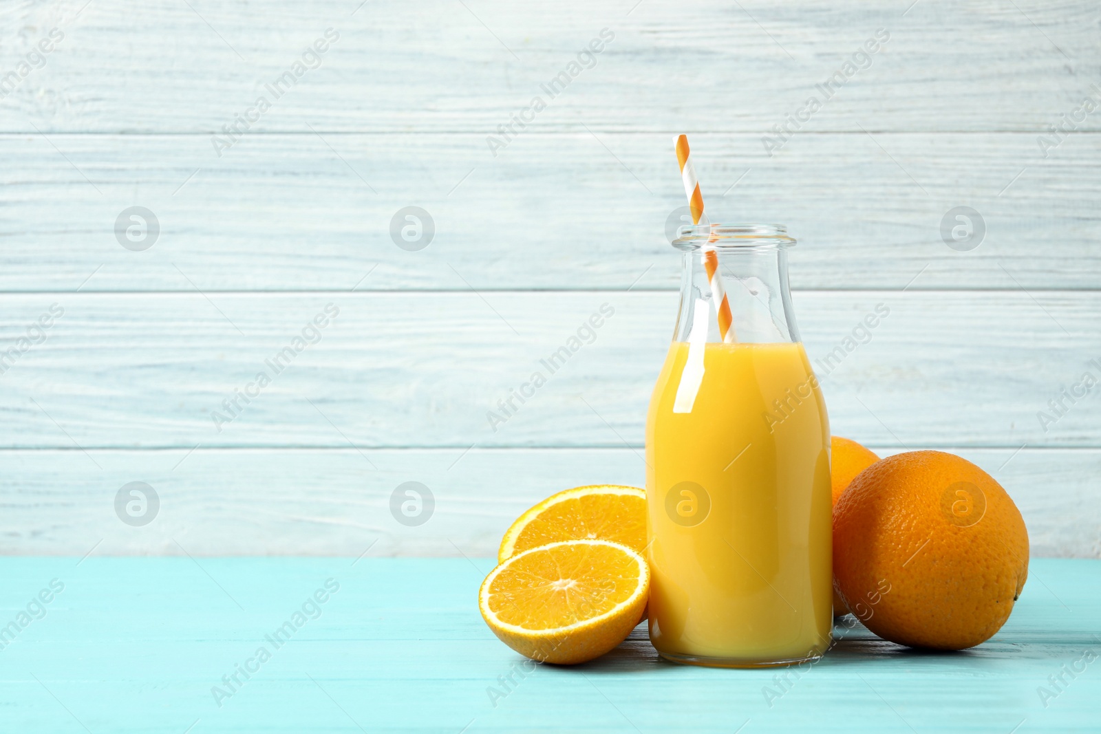 Photo of Bottle of orange juice and fresh fruits on light blue wooden table. Space for text