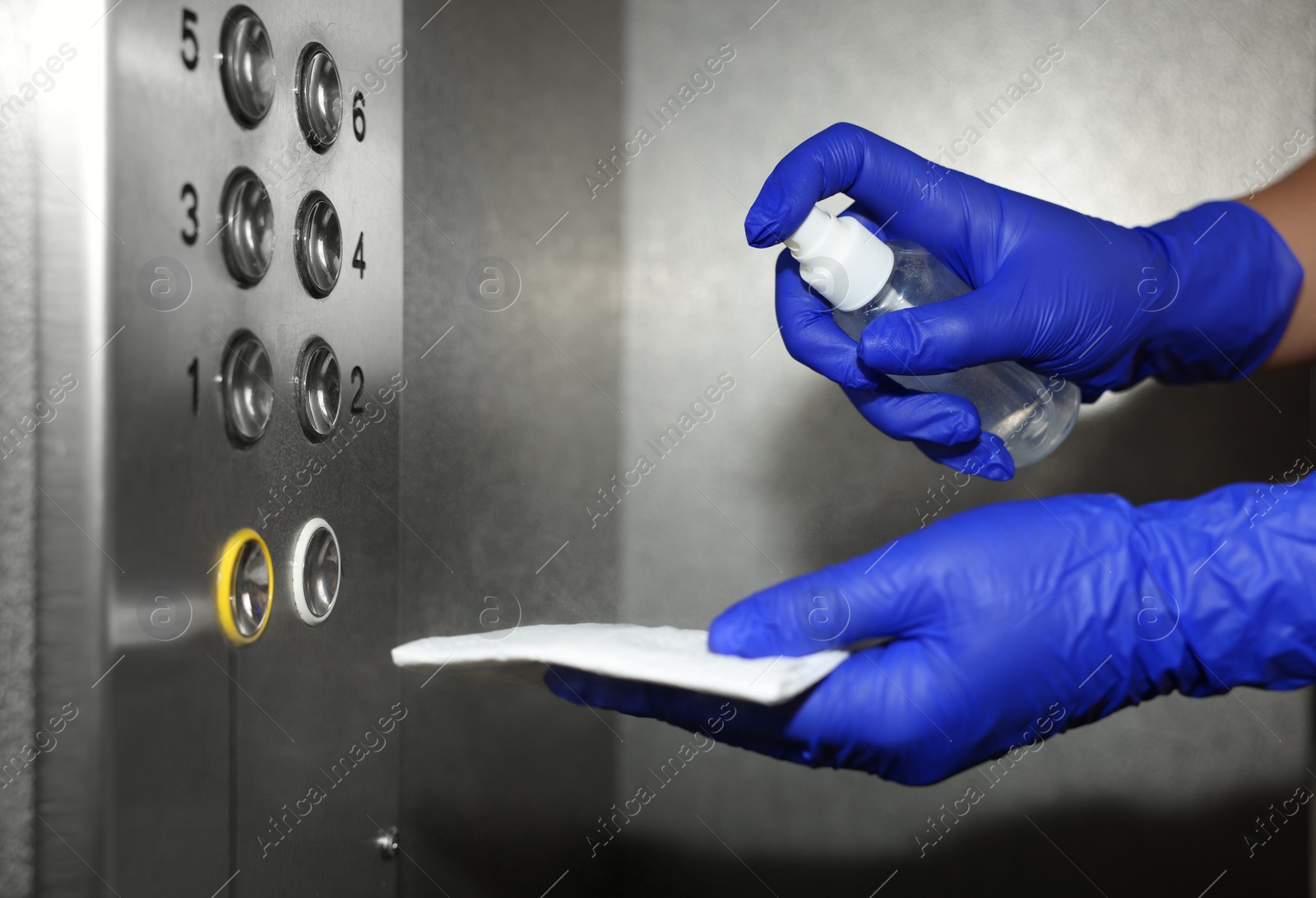 Photo of Woman with detergent spray and paper napkin cleaning elevator`s panel, closeup