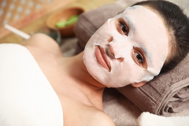 Beautiful woman with cotton mask sheet on face relaxing in spa salon, closeup