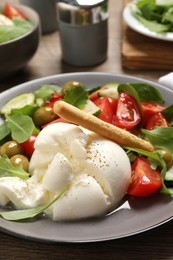 Photo of Delicious burrata salad served on wooden table, closeup