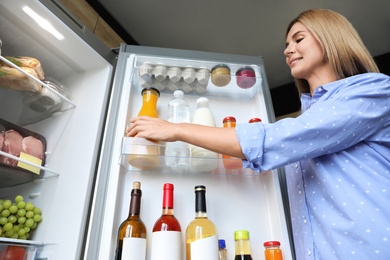 Woman taking bottle with juice out of refrigerator in kitchen