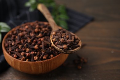 Bowl and spoon with aromatic cloves on wooden table, closeup. Space for text