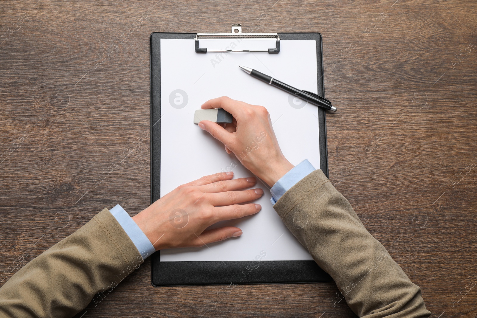 Photo of Woman erasing something on paper at wooden table, closeup