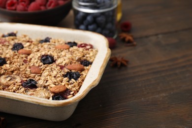 Photo of Tasty baked oatmeal with berries and almonds on wooden table in baking tray, closeup. Space for text