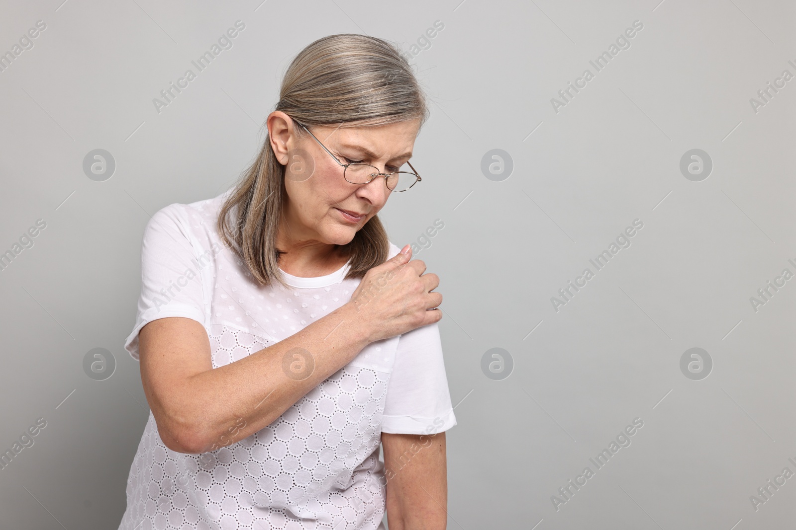 Photo of Arthritis symptoms. Woman suffering from pain in shoulder on gray background, space for text