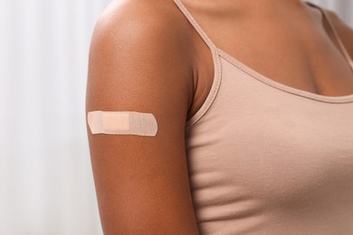 Photo of Young woman with adhesive bandage on her arm after vaccination against blurred background, closeup